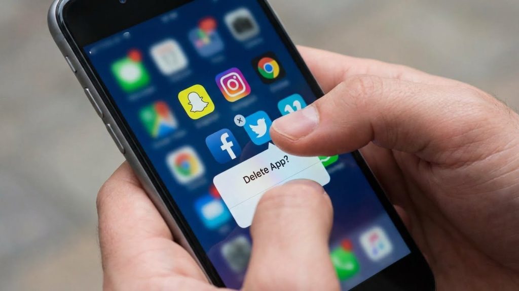 Pessoa a apagar aplicações de redes sociais do telemóvel ilustrando abandono progressivo de plataformas digitais