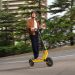 Xiaomi Electric Scooter 6 Ultra em cor amarela estacionada numa rua urbana, ao lado do Xiaomi Watch 5 no pulso de um utilizador