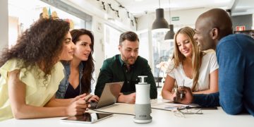 Dispositivo RICOH Meeting Hub 360 numa sala de reuniões híbrida com participantes presenciais e remotos