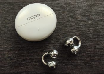 OPPO Enco Clip 2 em cinzento sobre superfície neutra, com o estojo de carregamento aberto ao lado, mostrando o design de clipe em liga de memória de forma NiTi