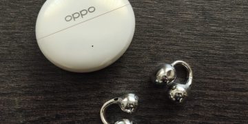 OPPO Enco Clip 2 em cinzento sobre superfície neutra, com o estojo de carregamento aberto ao lado, mostrando o design de clipe em liga de memória de forma NiTi