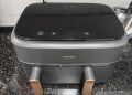 Philips Air Fryer Série 3000 Cesta Dupla NA352/00 em cinzento mate com detalhes metálicos dourados sobre bancada de cozinha moderna, com as duas gavetas abertas e o ecrã táctil iluminado