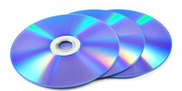 Disco Blu-ray com reflexo de luz azul sobre fundo escuro, ao lado de uma caixa de filme em formato físico